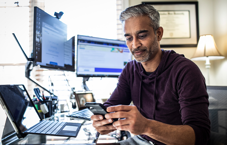 person sitting at their computer and looking at their phone